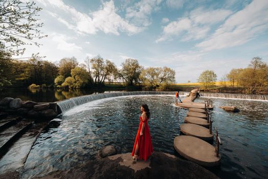 girl in a long red dress near the lake in the Park at sunset