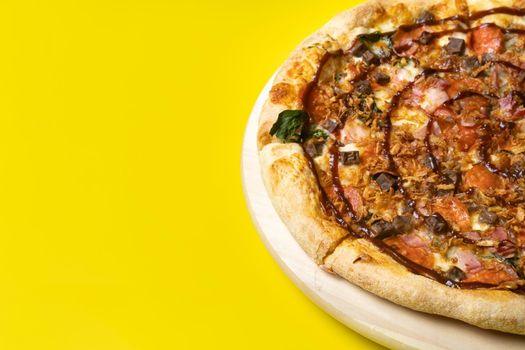 Delicious large pizza with bacon and spinach on a yellow background.