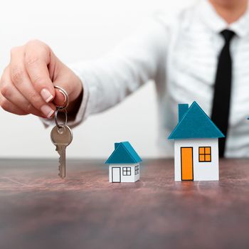 Businesswoman holding keys. olored paper houses standing on desk.