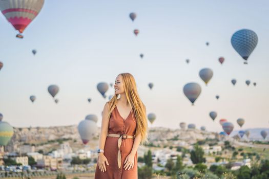 Tourist woman looking at hot air balloons in Cappadocia, Turkey. Happy Travel in Turkey concept. Woman on a mountain top enjoying wonderful view.
