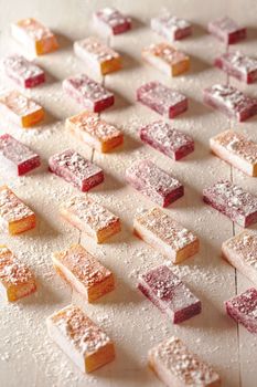 Delicious fruit and berry flavored jelly candies sprinkled with powdered sugar arranged on white wooden table. Concept of healthy natural sweets