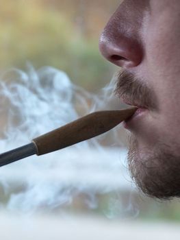 young man smoking a pipe, close-up side view.