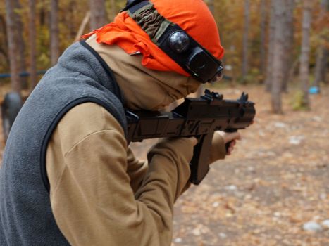 a teenager aiming aim at a laser gun while playing in the forest, rear view.