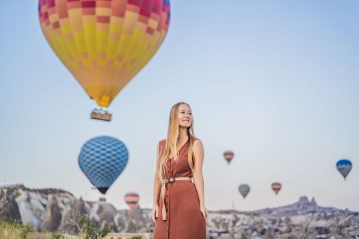 Tourist woman looking at hot air balloons in Cappadocia, Turkey. Happy Travel in Turkey concept. Woman on a mountain top enjoying wonderful view.