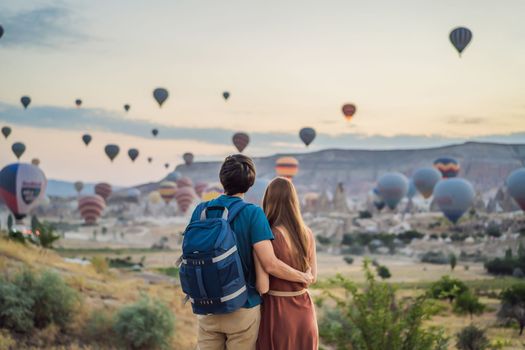 Tourists couple man and woman looking at hot air balloons in Cappadocia, Turkey. Happy Travel in Turkey concept. Couple man and woman on a mountain top enjoying wonderful view.