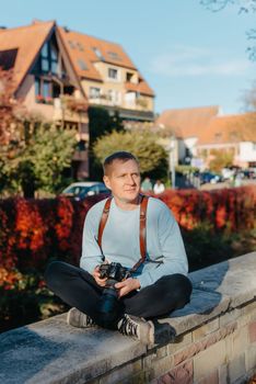 Man Sitting on Stairs in Old European City And Holding Photo Camera. Contemporary Stylish Blogger And Photographer