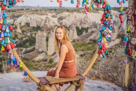 Young woman exploring valley with rock formations and fairy caves near Goreme in Cappadocia Turkey. Wish tree. Small multi-colored jugs with inscriptions, wishes hanging on the branches of a tree., against the backdrop of sand ruins and blue sky.