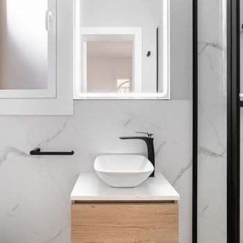 Bright bathroom boasts a sleek and minimalist style, featuring a gleaming white sink set against a stunning black framed mirror, creating a modern and sophisticated look