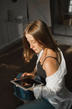 Portrait of young beautiful woman near window with shadow with digital tablet. Morning spring aesthetics and social networks digital technologies