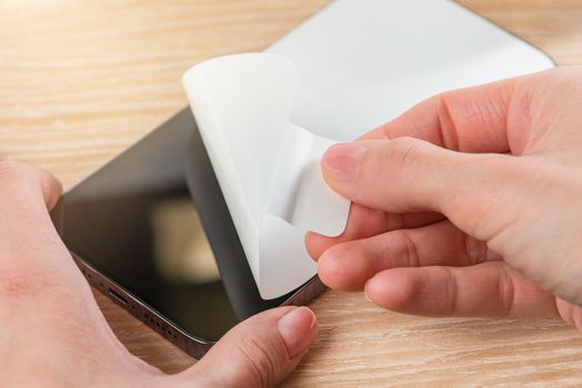 Unpacking a new phone. Remove the protective white film from the new phone. Close-up of a woman's hands removing a protective film from a phone in a purple case. Copy space on wooden table background