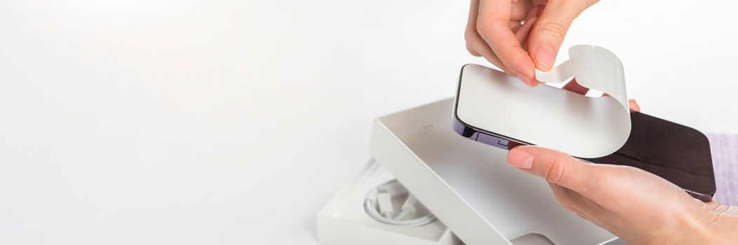 Unpacking a new phone. Remove the protective white film from the new phone. Close-up of a woman's hands removing a protective film from a phone in a purple case. Copy space on white background