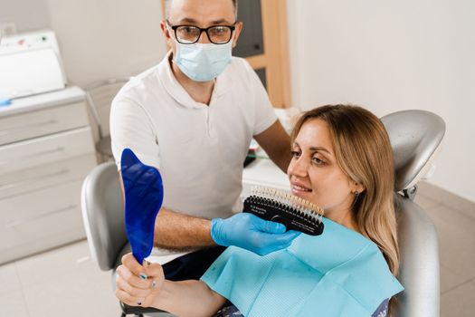 Teeth whitening. Patient looking at teeth color shades guide. Dentistry. Doctor checking tooth color matching samples in dental clinic