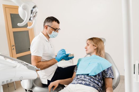 Dental prosthetics consultation with dentist for patient woman in dentistry. Doctor dentist shows artificial plastic jaw with dental implants