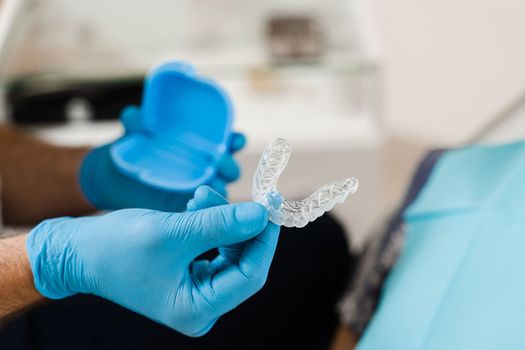 Clear aligner for bite correction and shape of teeth close-up. Orthodontist shows transparent removable retainer for patient woman in dentistry