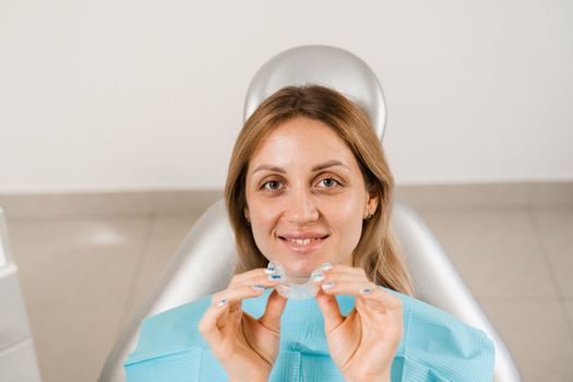 Clear aligner for bite correction and shape of teeth. Orthodontist shows transparent removable retainer for patient woman in dentistry