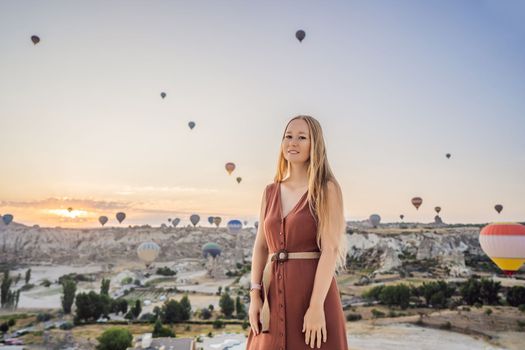 Tourist woman looking at hot air balloons in Cappadocia, Turkey. Happy Travel in Turkey concept. Woman on a mountain top enjoying wonderful view.