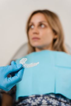 Clear aligner for bite correction and shape of teeth close-up. Orthodontist shows transparent removable retainer for patient woman in dentistry