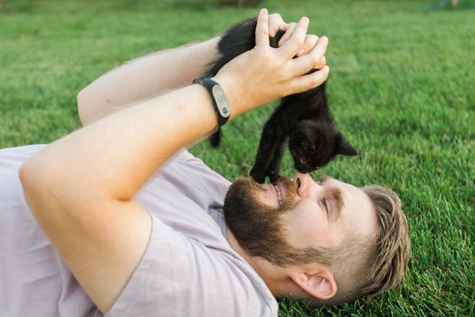 Man with little kitten lying and playing on grass - friendship love animals and pet owner