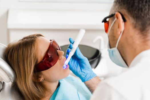 Uv illumination of photopolymer tooth filling procedure. Dentist in red protective glasses treats and removes caries in woman patient