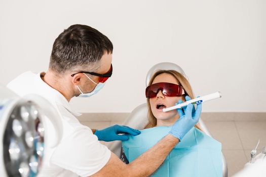 Uv illumination of photopolymer tooth filling procedure. Dentist in red protective glasses treats and removes caries in woman patient