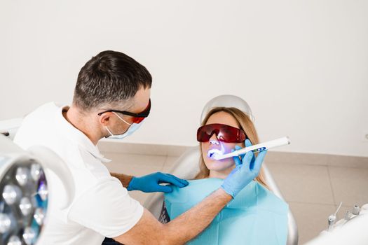 Uv illumination of photopolymer tooth filling for woman in dentistry. Dentist in red protective glasses treats and removes caries of girl patient