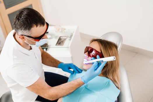 Uv illumination of photopolymer tooth filling for woman in dentistry. Dentist in red protective glasses treats and removes caries of girl patient