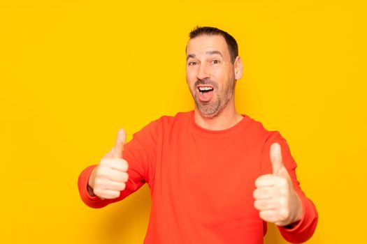 Attractive cheerful latino man with a beard wearing a red pullover standing isolated over yellow background, showing thumbs up