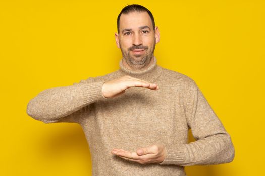 A man holding an object between his hands, showing, offering or advertising an object against an yellow wall. Empty. Space. Concept. Object. Bottom. Portrait. Copy.