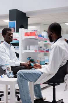 African american pharmacist measuring patient blood sugar with glucometer, pharmacy professional consultation. Glucose level measurement in drugstore, diabetes diagnosis, all black team