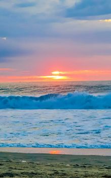 Beautiful stunning colorful and golden sunset in yellow orange red on beach and big wave panorama in tropical nature in Zicatela Puerto Escondido Oaxaca Mexico.