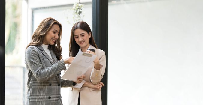 Two Asian businesswomen discussing, sharing their business ideas, reviewing financial report together...