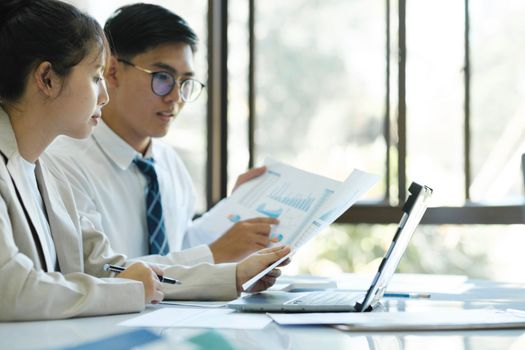 Businesspeople or colleagues are working together on project, discussing, sharing ideas, planning, and analyzing the business strategy and finance using laptop and graphs at workplace.