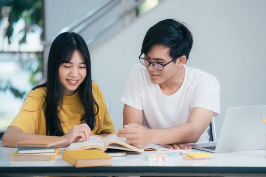 A Young man and woman are studying for an exam. There are tutor books with friends. They are classmates that try to help each other. They hat been tutoring for many hours in the campus.