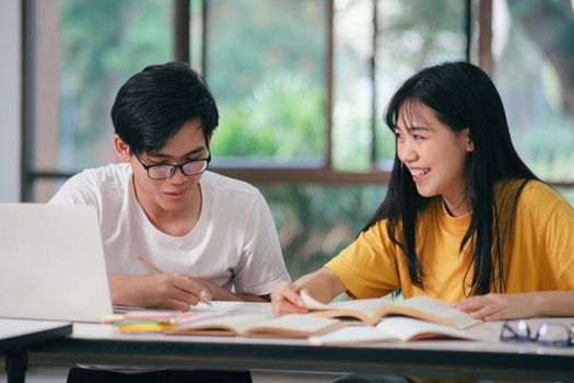 A Young man and woman are studying for an exam. There are tutor books with friends. They are classmates that try to help each other. They hat been tutoring for many hours in the campus.