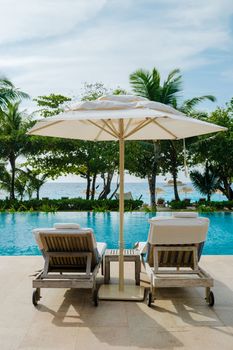 Beach chairs at a swimming pool at a luxury hotel, sun bed, and umbrella.