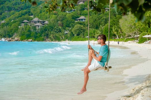 Young men relaxing in a swing on the beach of Mahe Tropical Seychelles Islands.