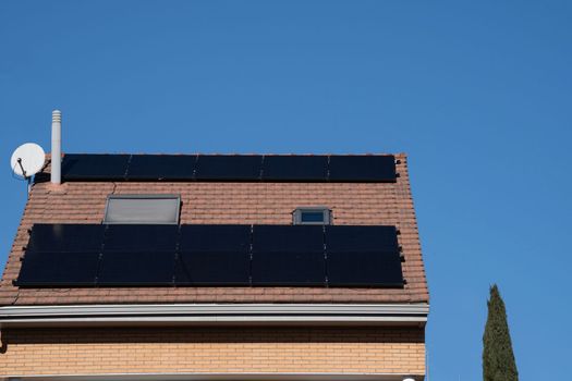 Black Photovoltaic panels on a roof of chalet house against clear blue sky.