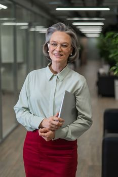 Attractive mature caucasian woman holding laptop while standing in office