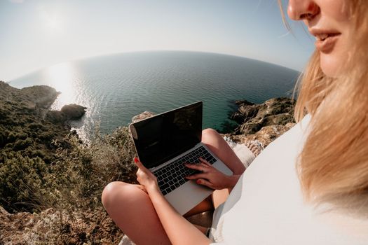 Woman sea laptop. Business woman in yellow hat working on laptop by sea. Close up on hands of pretty lady typing on computer outdoors summer day. Freelance, digital nomad, travel and holidays concept.