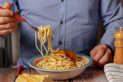 unrecognizable man in blue shirt with fork eating meatballs with spaghetti