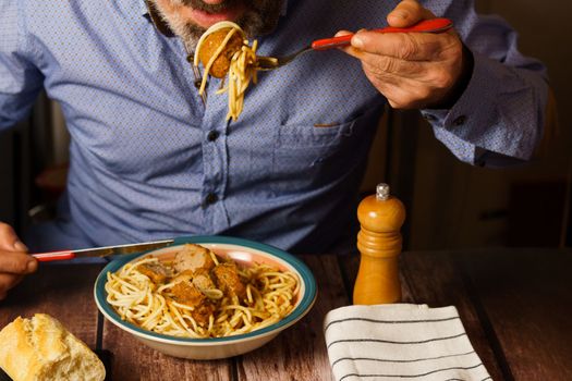 man with beard and blue shirt eating meatballs with spaghetti in a restaurant