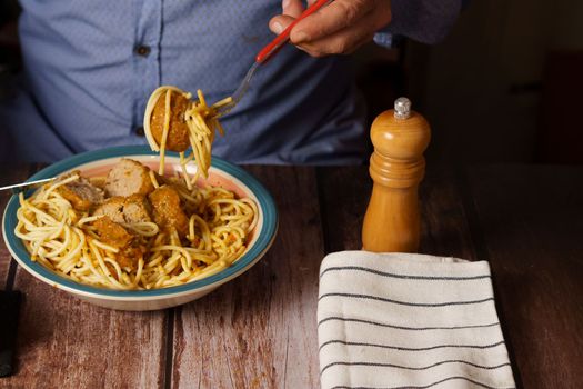 man with beard and blue shirt eating meatballs with spaghetti in a restaurant