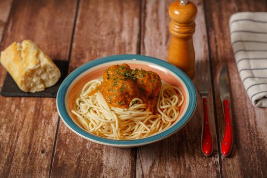 plate of meatballs with spaghetti with cutlery and bread and pepper shaker on a wooden table