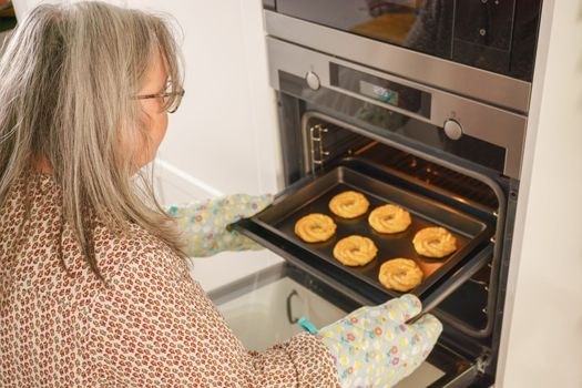 older white-haired woman putting a tray of cookies in the oven