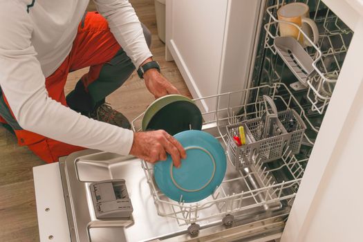 man in white t-shirt putting the dishes in the dishwasher, in the kitchen of his house