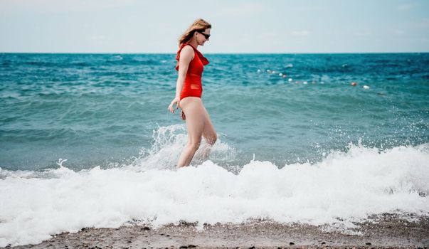 Young happy woman walks carefree on the seaside. Happy lady in red bikini. Portrait beautiful young woman relax smile around beach sea ocean in holiday vacation travel trip.