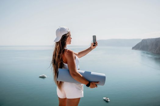 Young woman with black hair, fitness instructor in pink sports leggings and tops, doing pilates on yoga mat with magic pilates ring by the sea on the beach. Female fitness daily yoga concept