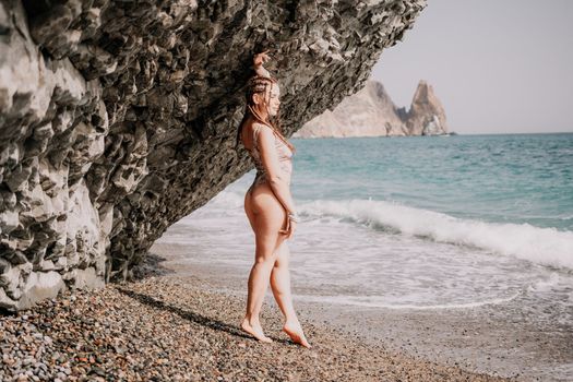 Beach vacation. Hot beautiful woman in sunhat and bikini standing with her arms raised to her head enjoying looking view of beach ocean on hot summer day.