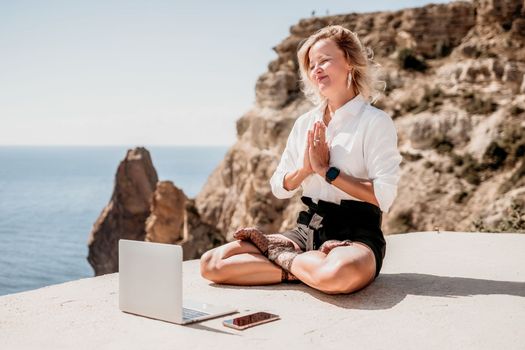 Happy girl doing yoga with laptop working at the beach. beautiful and calm business woman sitting with a laptop in a summer cafe in the lotus position meditating and relaxing. freelance girl remote work beach paradise