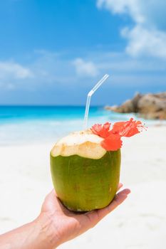 Coconut drink in palm hand on a tropical beach La Digue Seychelles Islands.